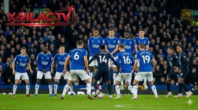 Góc quay trên cao chiến thuật trận Everton vs Chelsea với cầu thủ Everton bị marqués giữa sân và logo XOILAC TV lớn màu đỏ. Điểm số là 1-1.