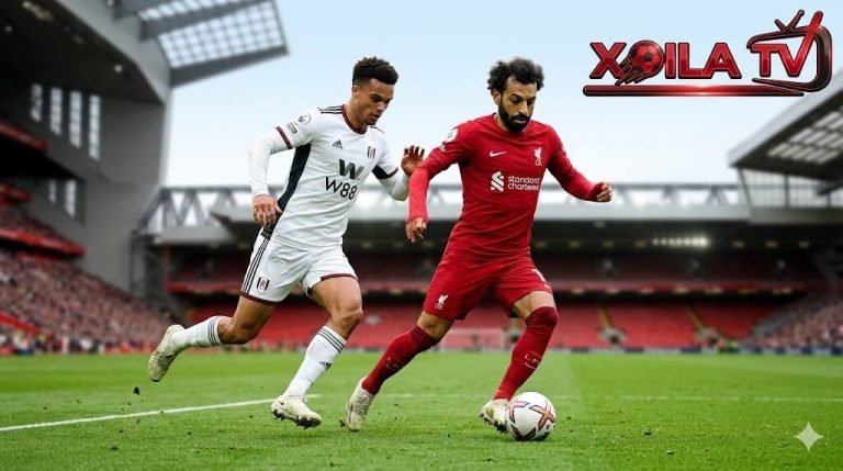 Ảnh hành động góc thấp ghi lại cuộc đối đầu 1-1 căng thẳng giữa Mohamed Salah (áo đỏ Liverpool) đang dribbling bóng và Antonee Robinson (áo trắng Fulham) truy cản quyết liệt trên sân Anfield, với logo Xoilac TV ở góc. Điểm nóng định đoạt trận Liverpool vs Fulham vòng 32 Premier League.
